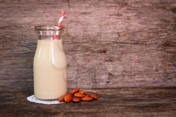 Almond milk in a  bottle with strip straw and fresh almond on a wooden surface