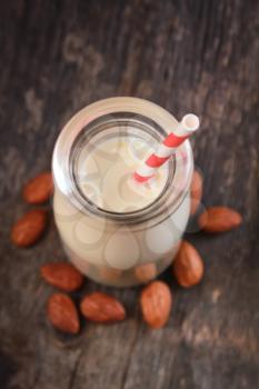 Top view of a bottle full of almond milk with red striped straw and fresh almonds on a wooden surface