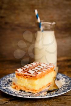 Millefeuille, french pastry with custard and bottle of milk with a blue straw on a wooden table