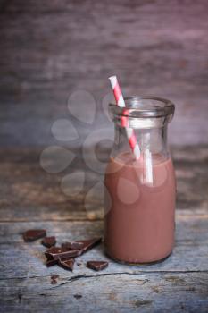 Old-fashionned bottle of chocolate milk with red striped straw and fresh dark chocolate on wooden background