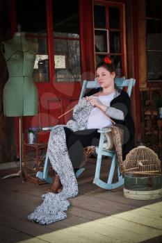 Smiling pregnant woman sitting on a rocking chair on a balcony and knitting