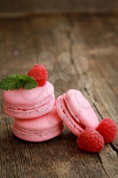 Three raspberry macarons on a wooden table with fresh fruits and mint
