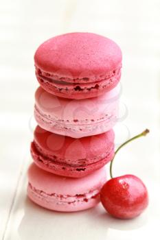 Row of four pink macarons on a white table with fresh fruits 