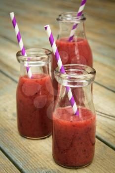 Berry smoothie freshly made in a jar with a lined straw on rustic wood
