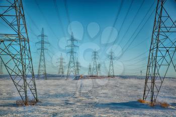 Group of high-voltage electricity power pylons over blue sky and snow covered countryside, Canada