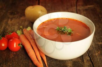 Vegetables soup surrounded by fresh vegetables on a rustic background