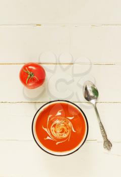 Tomato soup with spoon on a white wooden background