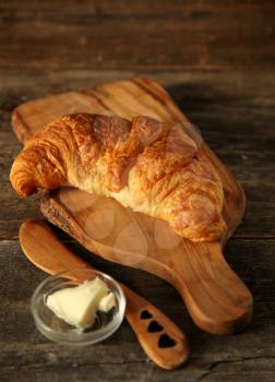 Fresh homemade croissant on a cupboard with butter and wooden knife