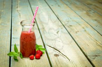 Strawberry smoothie freshly made in a jar with a straw on rustic wood