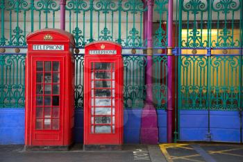 Two red booths in two different sizes with green and blue iron fence in background in Smithfield market in London UK
