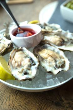 Tasty fresh oysters on ice with sliced juicy lemon on plate