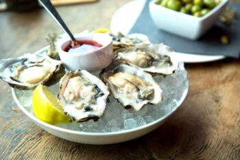 Tasty fresh oysters on ice with sliced juicy lemon on plate