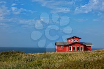 Red house in a middle of a field in Magdalen island in Canada.  Image taken from the street.