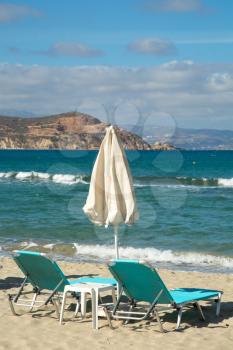 Turquoise sunbathing chairs on a beach with turquoise ocean and coastline in Greece
