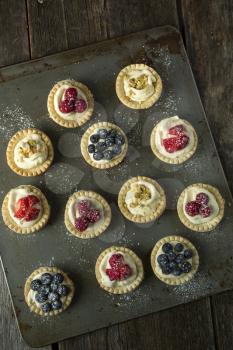 Top view of blueberry, strawberry and pistachios tartlets on  biscuit sheet on a  wooden table