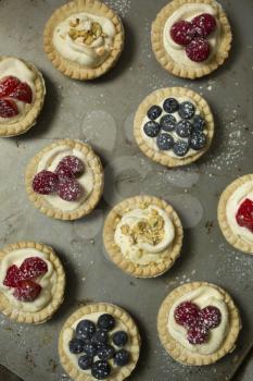 Top view of blueberry, strawberry and pistachios tartlets on  biscuit sheet on a  wooden table