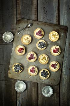 Top view of blueberry, strawberry and pistachios tartlets and aluminum plate on biscuit sheet on a wooden table