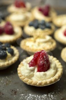 Strawberry, blueberry and pistachios tartlets on biscuit sheet on a wooden table