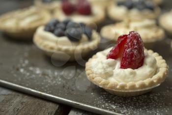 Blueberry, strawberry and pistachios tartlets on biscuit sheet on a wooden table