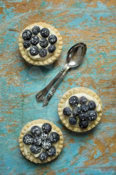 Top view of blueberry tartlets with spoons on a grunge background