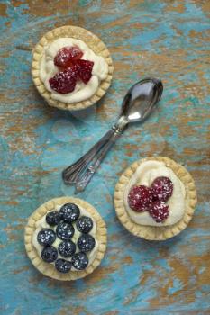 Top view of berries tartlets with spoons on a grunge background