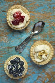 Top view of berries and pistachios tartlets with spoons on a grunge background