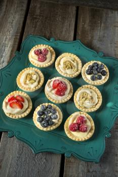 Strawberry, blueberry and pistachios tartlets on green tray on a wooden table