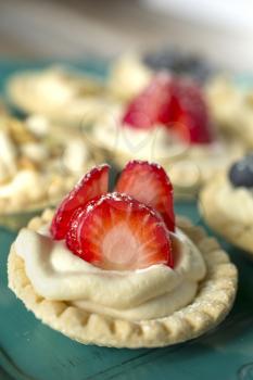 Strawberry, blueberry and pistachios tartlets on green tray on a wooden table