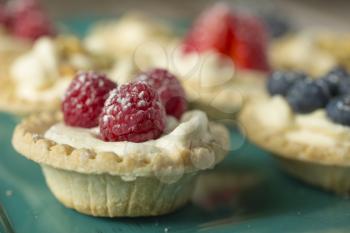 Raspberry, blueberry and pistachios tartlets on green tray on a wooden table