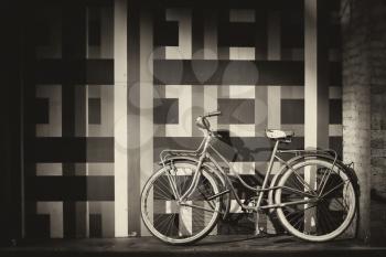 vintage bicycle along a wall with geometric pattern.  Picture in sepia