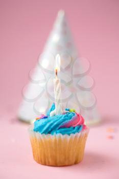 Cupcake with blue and pink icing and birthday hat on a pink background
