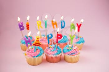 Cupcakes with blue and pink icing and happy birthday candles on a blue background