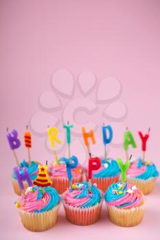 Cupcakes with blue and pink icing and happy birthday candles on a blue background