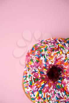 Close up of a donut with pink icing and candies on a pink pastel background