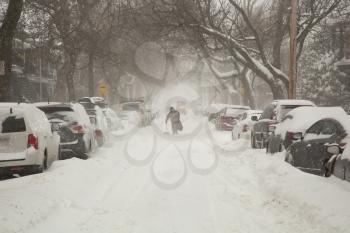 Man with shovel walking in a street covered of snow and cars full of snow in a street during a snowstorm in Montreal in  Canada