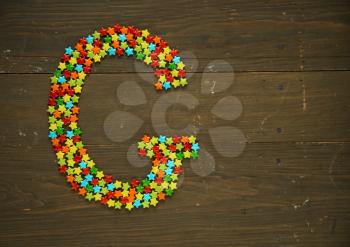 Letter G from alphabet made with star shape candy on a wooden background