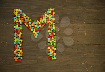 Letter M from alphabet made with star shape candy on a wooden background