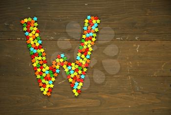 Letter W from alphabet made with star shape candy on a wooden background