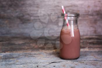 Bottle of chocolate milk with red striped straw on wooden background
