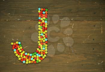 Letter J from alphabet made with star shape candy on a wooden background