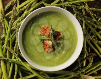 Asparagus soup surrounded by fresh vegetables on a wooden background