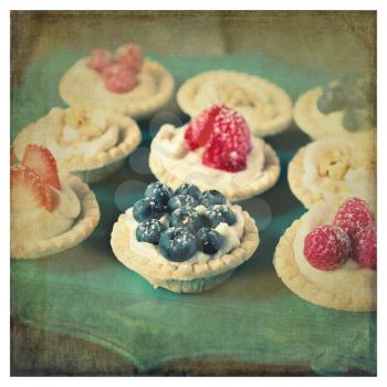 Strawberry, blueberry and pistachios tartlets on green tray with retro style and texture 